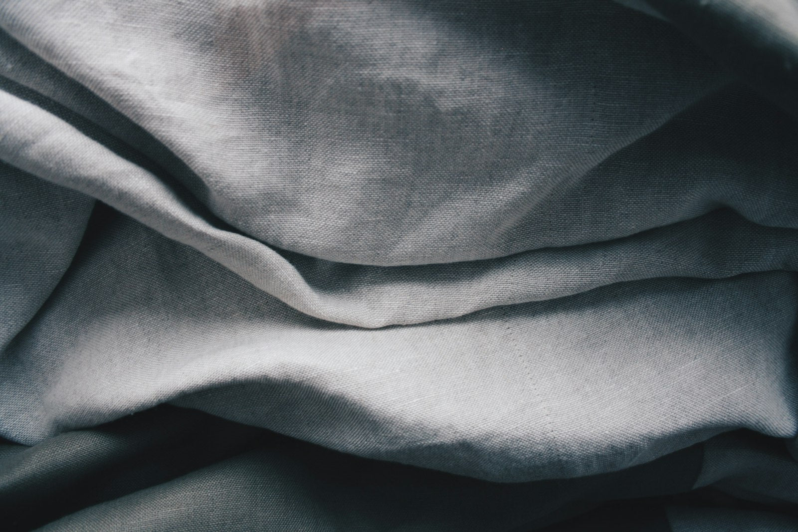 Soft folds of natural grey linen fabric in close-up, illustrating the texture of an unembellished natural fiber.