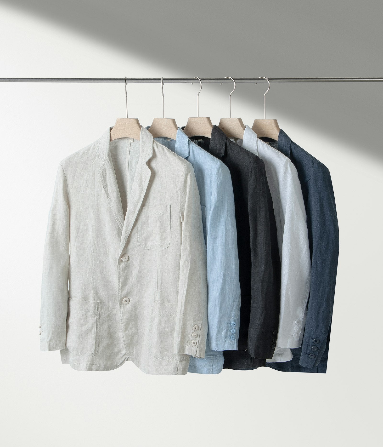A row of neutral-toned shirts hanging on a wooden clothes rack, representing a curated slow fashion wardrobe